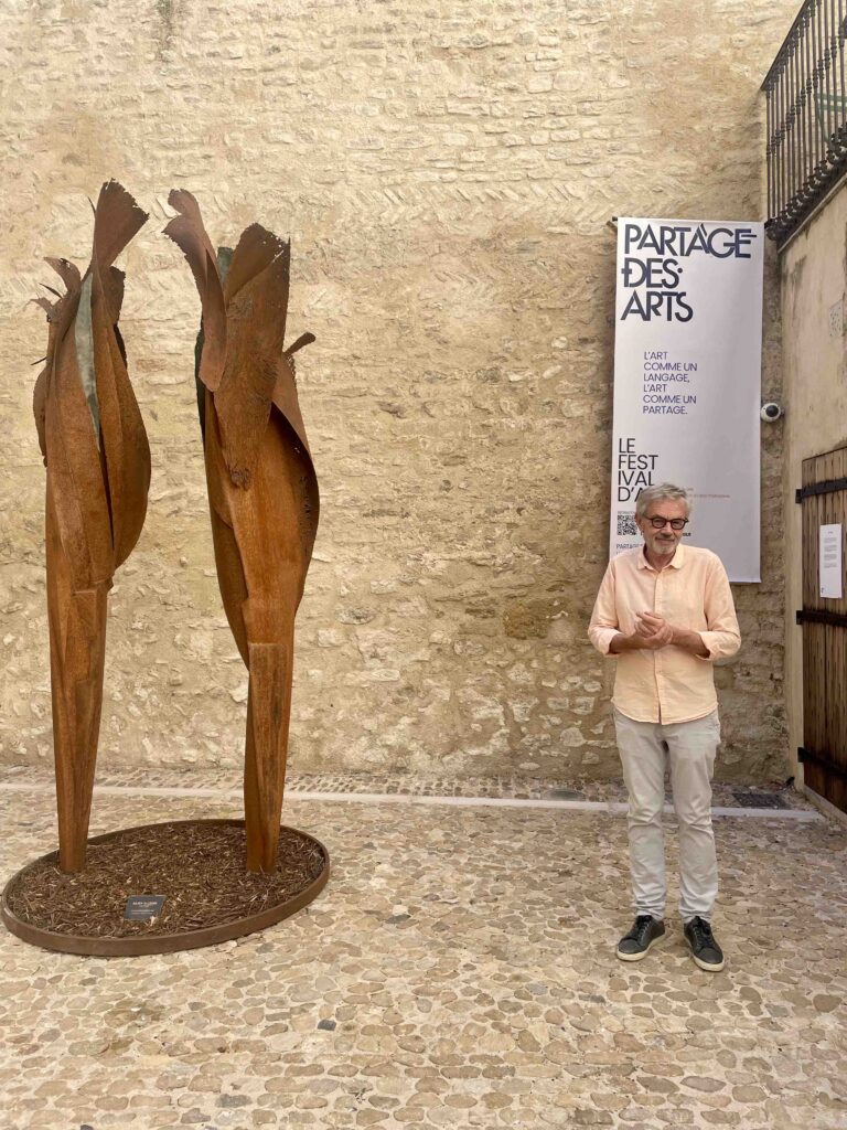 Bruno poyet fondateur su festival partage des arts de l'isle sur la sorgue devant deux scultures de julien allègre